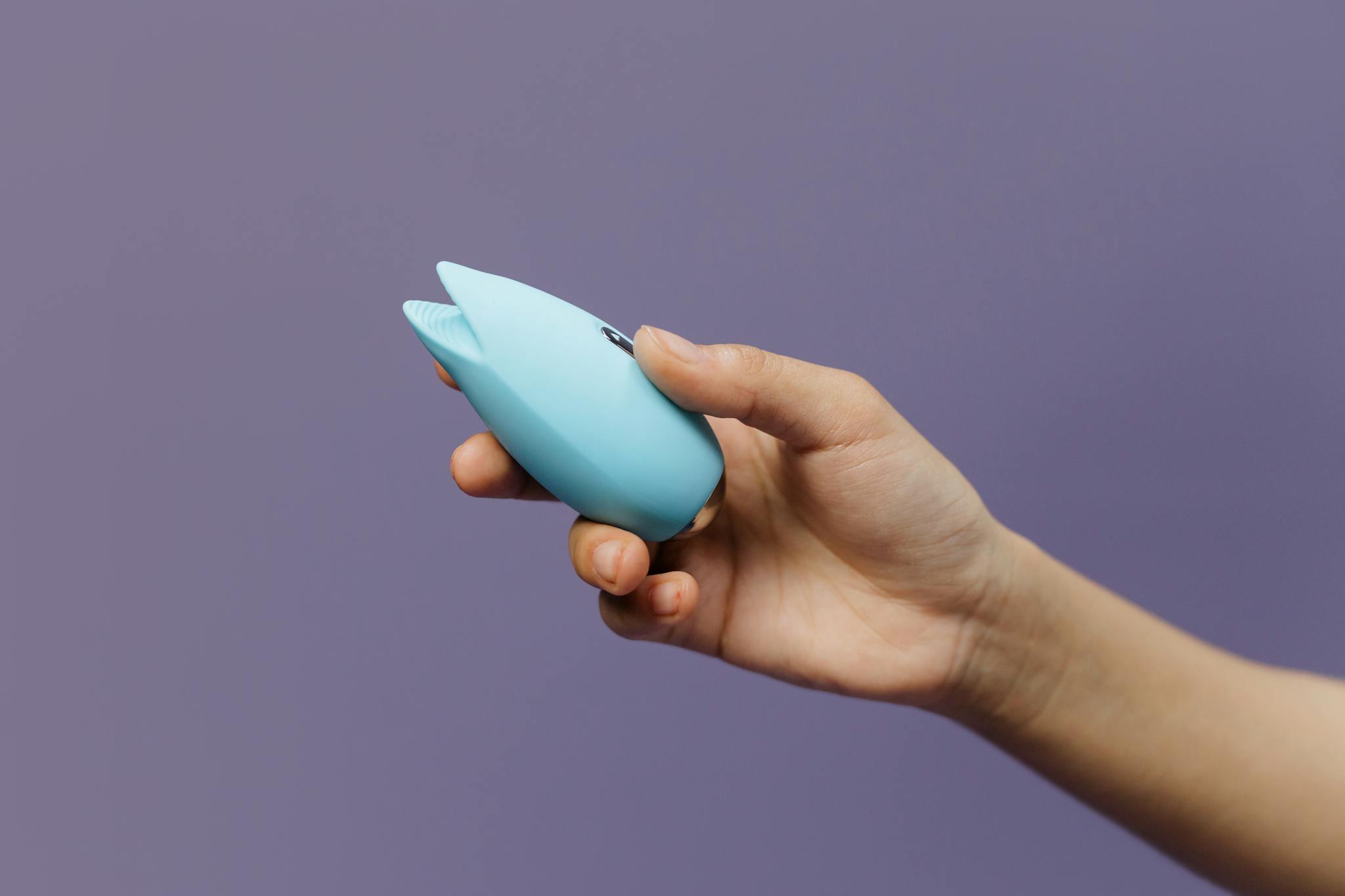 A blue silicone sex toy held in hand against a solid purple background, promoting self-love and sexuality.