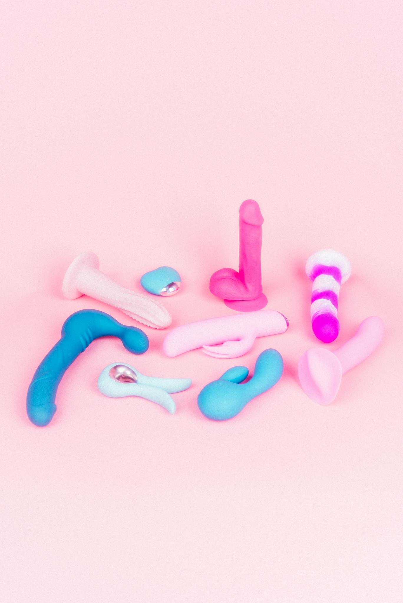 A variety of vibrators and sex toys in bright colors on a pink backdrop.