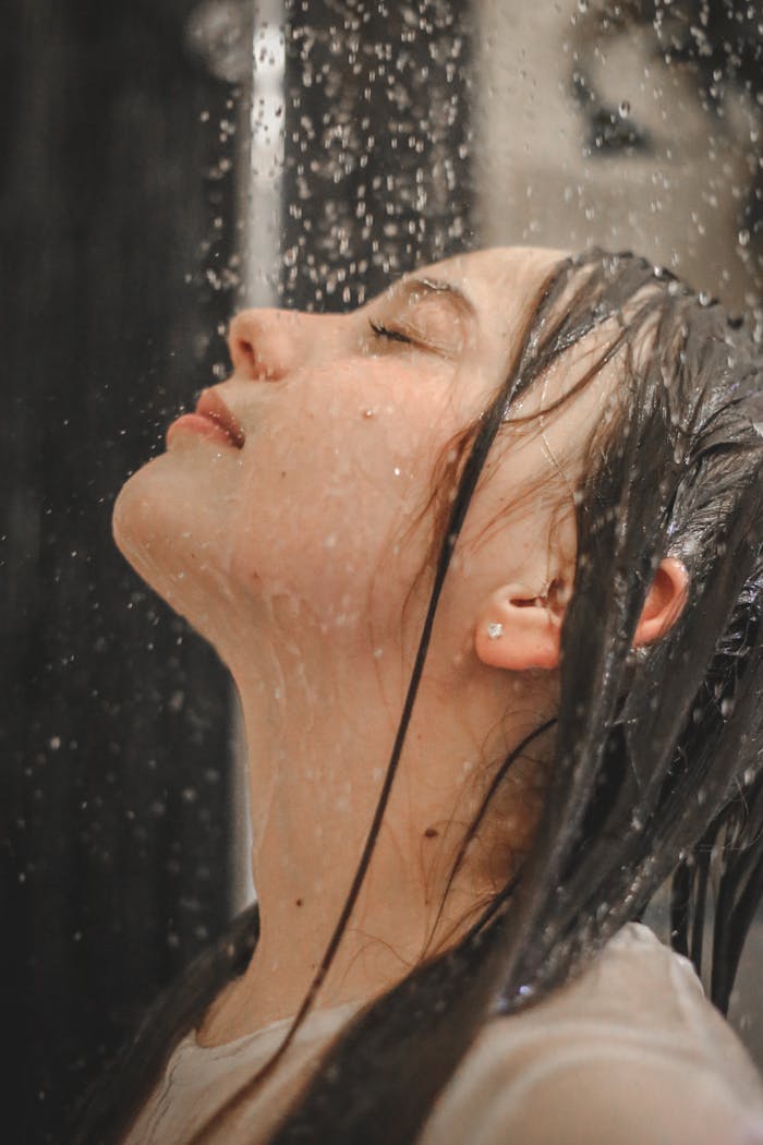 Graceful side profile of a woman embracing the rain shower indoors.