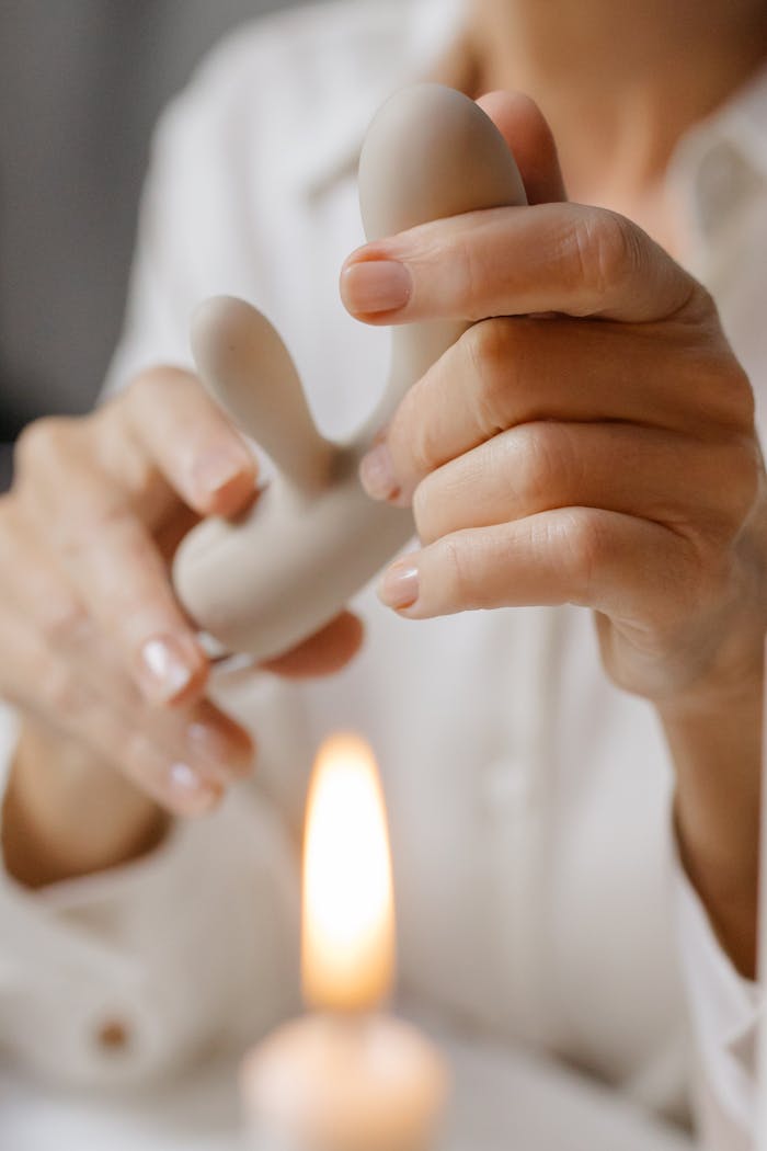 Hands gently holding a rabbit vibrator with a lit candle in the background, depicting intimacy and self-care.